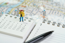 Miniature Traveller, Backpacker Man Figure Standing On Calendar With Pen And Map Using As Travel Planning Or Year Vacation Or Holiday