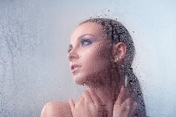 brunette woman with makeup smoky eyes hugging his neck behind glass with water drops and close-up in profile