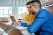 © Seventyfour - Portrait of two students sitting at desk in modern auditorium at college and preparing for class, focus on young Middle-Eastern man using laptop