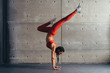 Young fit woman doing handstand exercise in studio.