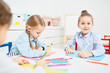 © pressmaster - Group of little girls sitting by table in kindergarten and drawing with crayons