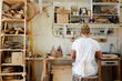 © pressmaster - Back view of young contemporary artisan sitting by workplace on stump seat
