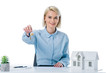 © LIGHTFIELD STUDIOS - portrait of smiling real estate agent showing keys at workplace with house model isolated on white