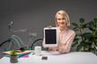 © LIGHTFIELD STUDIOS - portrait of smiling businesswoman showing tablet at workplace isolated on grey
