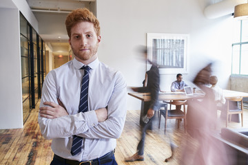 Wall Mural - Portrait of young red haired man in a busy modern workplace