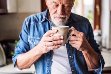 Senior man holding a cup of coffee in the kitchen.