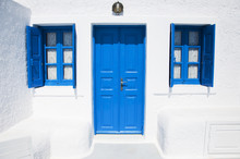Traditional Greek Architecture With Blue Doors And Bright Blue Shutters On The Island Of Santorini, Greece, Europe. The Famous White Greek Architecture.