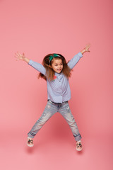 Wall Mural - Full-length picture of joyful carefree child jumping and throwing hands up in the air being isolated over pink background