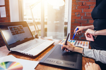 Wall Mural - close-up image of women drawing a project using a graphic tablet and a laptop sitting in modern offi