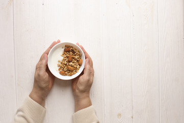 Wall Mural - Woman eating homemade granola breakfast cereals with mixed nuts, oats and Greek yogurt in bowl. Female hands holding healthy vegetarian food with cashew, almond, hazelnut. Morning light, copy space.