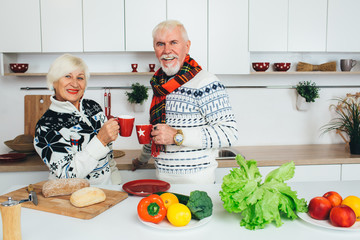 Elderly happy couple drinking tea standing at home in the kitchen, seniors people spending time together at home.