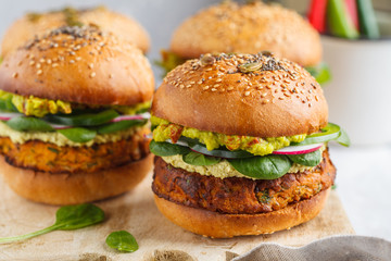 Healthy baked sweet potato burger with whole grain bun, guacamole, vegan mayonnaise and vegetables on a wooden board. Vegetarian food concept, light background.