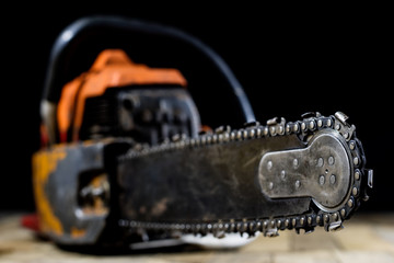 An old power saw for cutting wood. Chainsaw and protective clothing on a wooden workshop table.