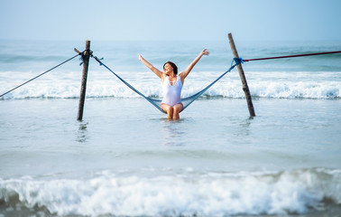 Wall Mural - Pretty woman enjoy with ocean breeze and sun sits in hammock swing over the waves