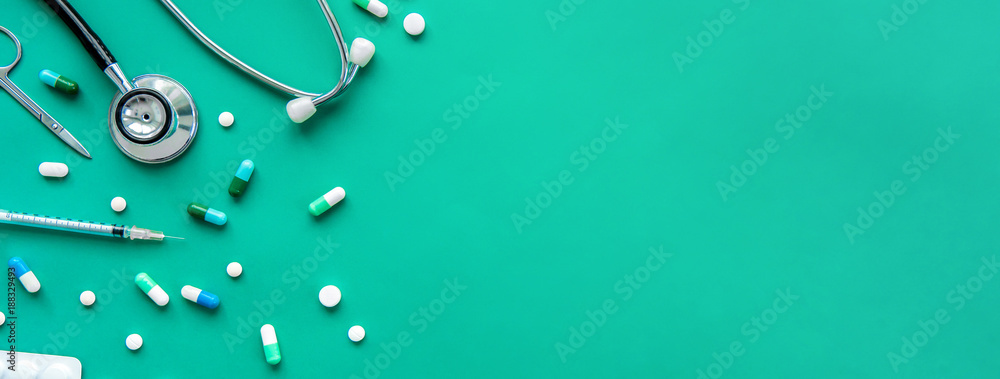 Pills and medical equiupments including stethoscope, syringe and scissors at border on green banner background, top view with copy space - obrazy, fototapety, plakaty 