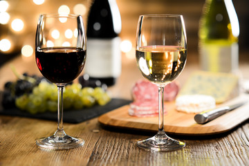 two glass of red wine and white wine with french cheese and delicatessen in restaurant wooden table with romantic dim light and cosy atmosphere