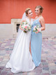 Stunning bride and bridesmaid in blue dress have fun posing before an orange wall
