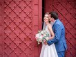 Gorgeous newlyweds kiss each other tender standing before red gates