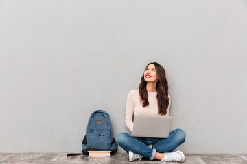 horizontal image of female looking upward while reading or communicating online using silver laptop 