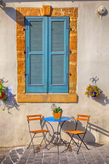 Sticker - Blue shutters window and beautiful small chairs and a table on sidewalk