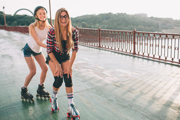 Two slim and sexy young women and roller skates. One female has an inline skates and the other has a quad skates. Girls ride in the rays of the sun