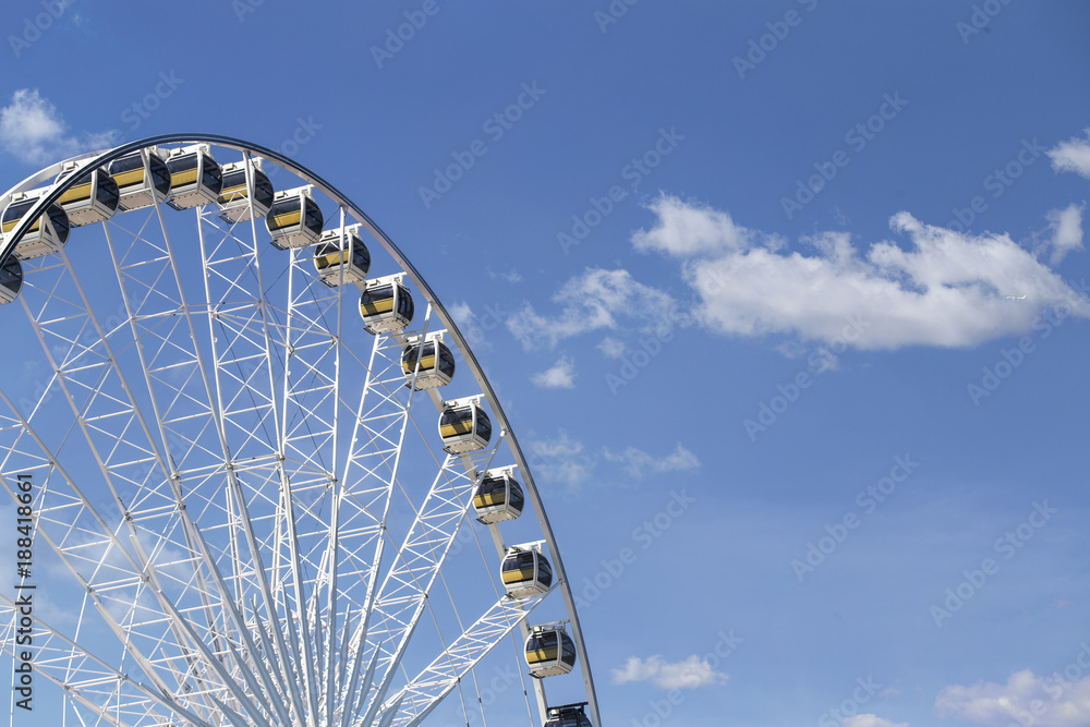 Giant Ferris wheel with numbered cabins in the park - Bright blue sky with sharp clouds behind it. - obrazy, fototapety, plakaty 