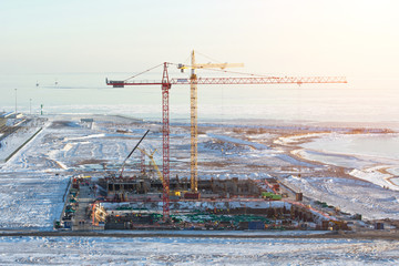 cranes at the construction site on the shore of the snow of the frozen sea in winter.