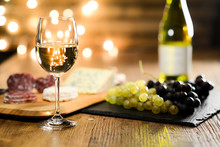 Glass Of White Wine With French Cheese And Delicatessen In Restaurant Wooden Table With Romantic Dim Light And Cosy Atmosphere