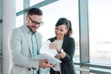 Two young business people talking about documents in office lobby.