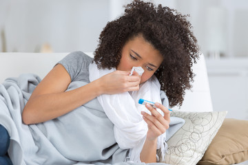 young sick woman in bed with thermometer looking bad