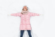 © Shopping King Louie - happy woman lying in the snow and moving arms and legs up and down, creating the shape of a snow angel. Smiling woman lying on snow in winter holiday ,for advertising ,