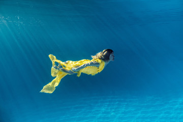 Wall Mural - underwater picture of beautiful young woman in dress swimming in swimming pool