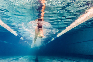 underwater picture of young swimmer in goggles exercising in swimming pool