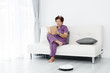 © nuiiko - Happy Asian senior woman reading a book at home, cleaning robot working.