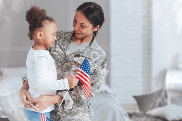 Patriotic family. Cheerful nice pleasant woman wearing a military uniform and looking at her daughter while getting ready to go on a mission