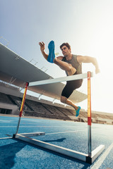 Wall Mural - athlete jumping over an hurdle on running track
