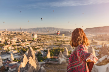 Wall Mural - A woman travels through Cappadocia at the background of a grandiose balloon show in Turkey