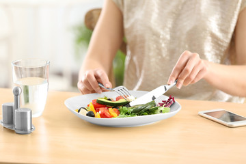 Wall Mural - Young woman eating fresh salad at table