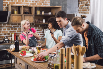 multiethnic girls drinking wine while men cooking in kitchen