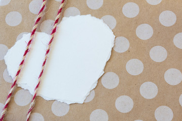 White torn paper heart on a brown polka dot surface with two lines of red and white twine across one side, copy space, horizontal aspect