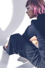 Wall Mural - side view of fashionable girl with pink hair sitting on white