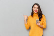 © Drobot Dean - Smiling brunette woman in sweater with smartphone pointing at copyspace