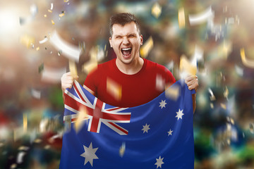 Wall Mural - Australian fan, a fan of a man holding the national flag of Australia in his hands. Soccer fan in the stadium. Mixed media