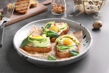 Tasty bruschettas with fried eggs and avocado on plate