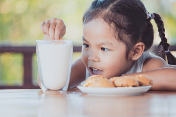 Cute asian little child girl eating cookie with milk for breakfast with happiness