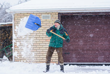 A Man Cleans Snow In Winter Weather With A Shovel Near The Garage 
