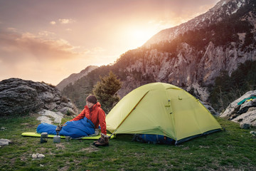 female traveler in sleeping bag near the tent in the mountains
