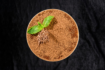 Poster - Traditional Italian sweet Tiramisu dessert in a glass witn mint leaves and cocoa on dark background. Top view, flat lay