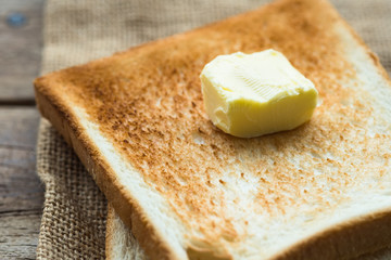 Wall Mural - piece of fresh butter on stacked toasted slice sandwich bread on gunny sack cloth on wooden table, close up