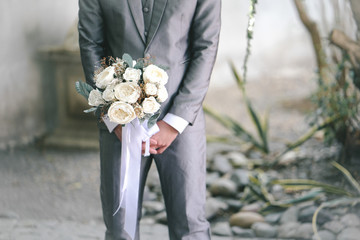 A man in grey suit hoding white roses bouquet in his hand.